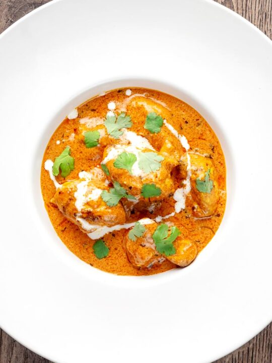 Portrait overhead image of murgh makhani or a butter chicken curry with a swirl of cream and fresh coriander served in a white bowl