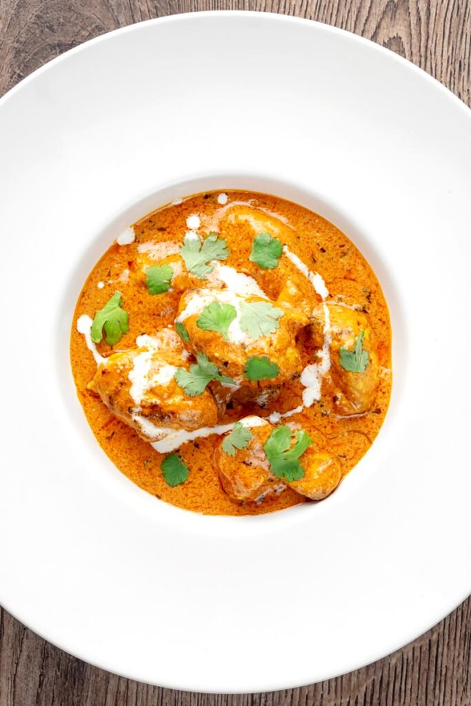 Portrait overhead image of murgh makhani or a butter chicken curry with a swirl of cream and fresh coriander served in a white bowl