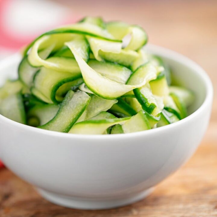 Square image of quick pickled cucumber ribbons served in a white bowl