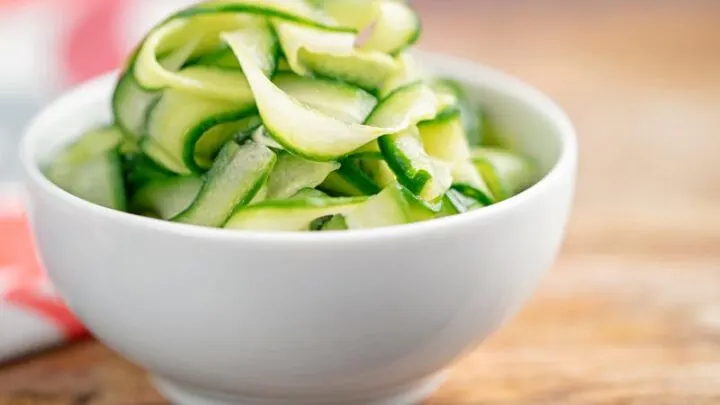 Landscape image of quick pickled cucumber ribbons served in a white bowl