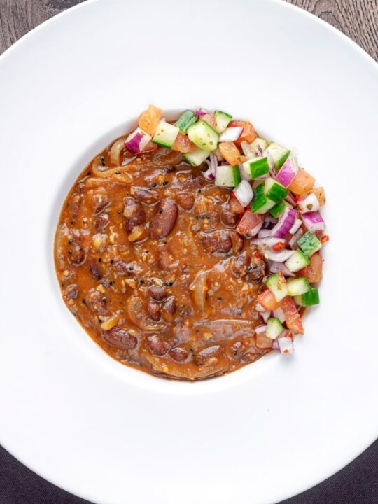 Portrait overhead image of a rajma masala kidney bean curry served with a kachumber salad in a white bowl