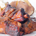 Close up portrait of char siu pork ribs that have been cooked in a slow cooker served with baked potatoes with text overlay