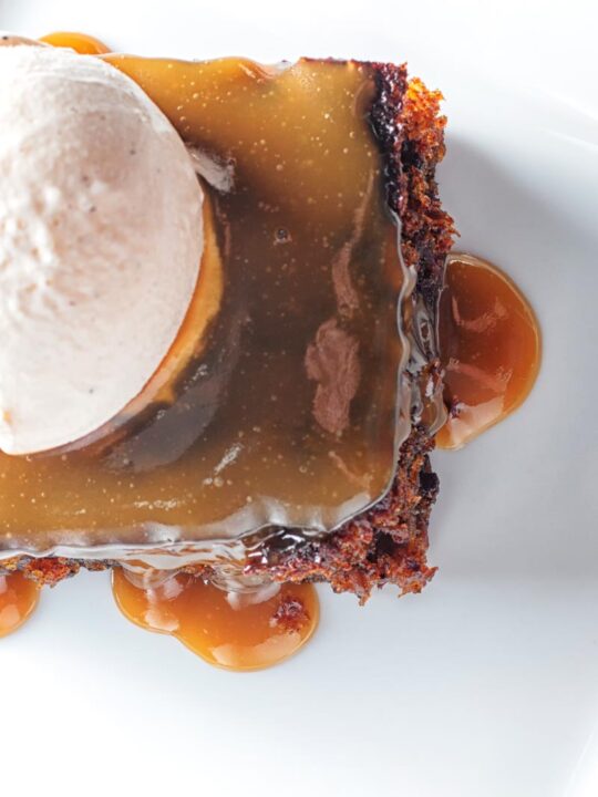 Portrait overhead image of a sticky toffee pudding topped with caramel sauce and vanilla ice cream