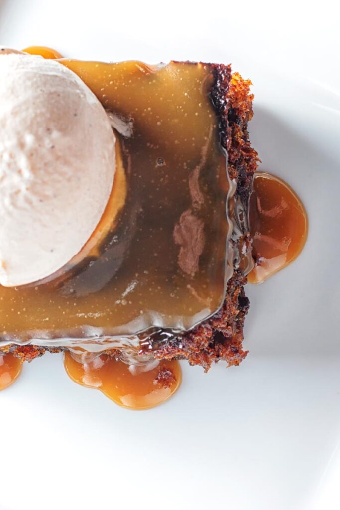 Portrait overhead image of a sticky toffee pudding topped with caramel sauce and vanilla ice cream