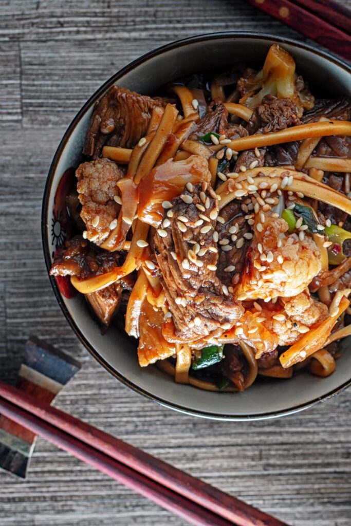 Portrait overhead image of Szechuan beef stir fry with noodles and cauliflower