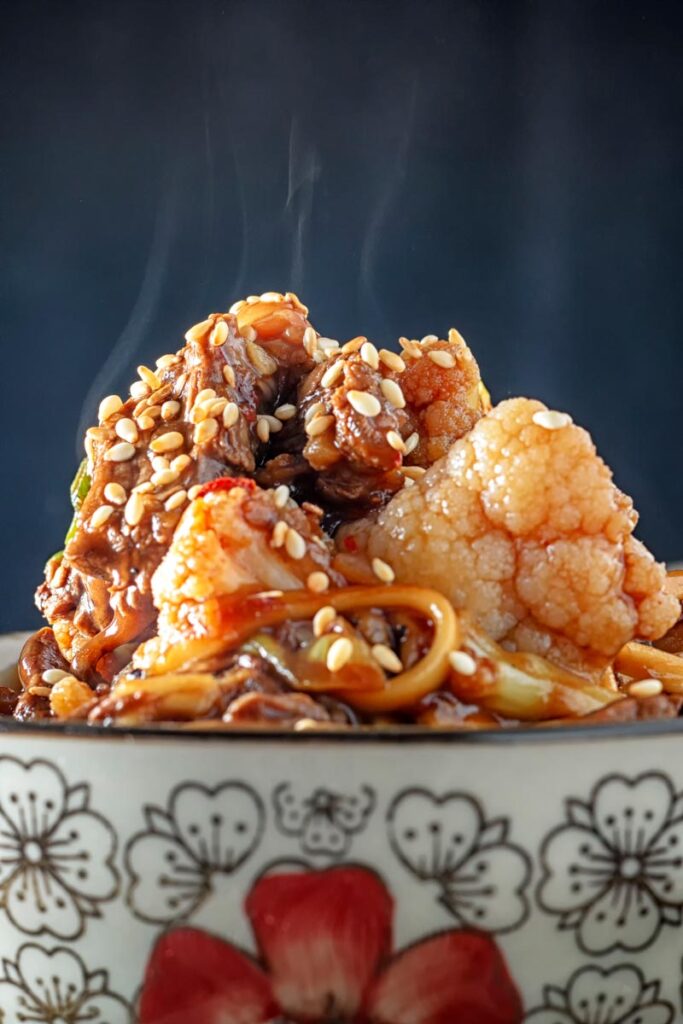 Portrait close up image of Szechuan beef stir fry with noodles and cauliflower