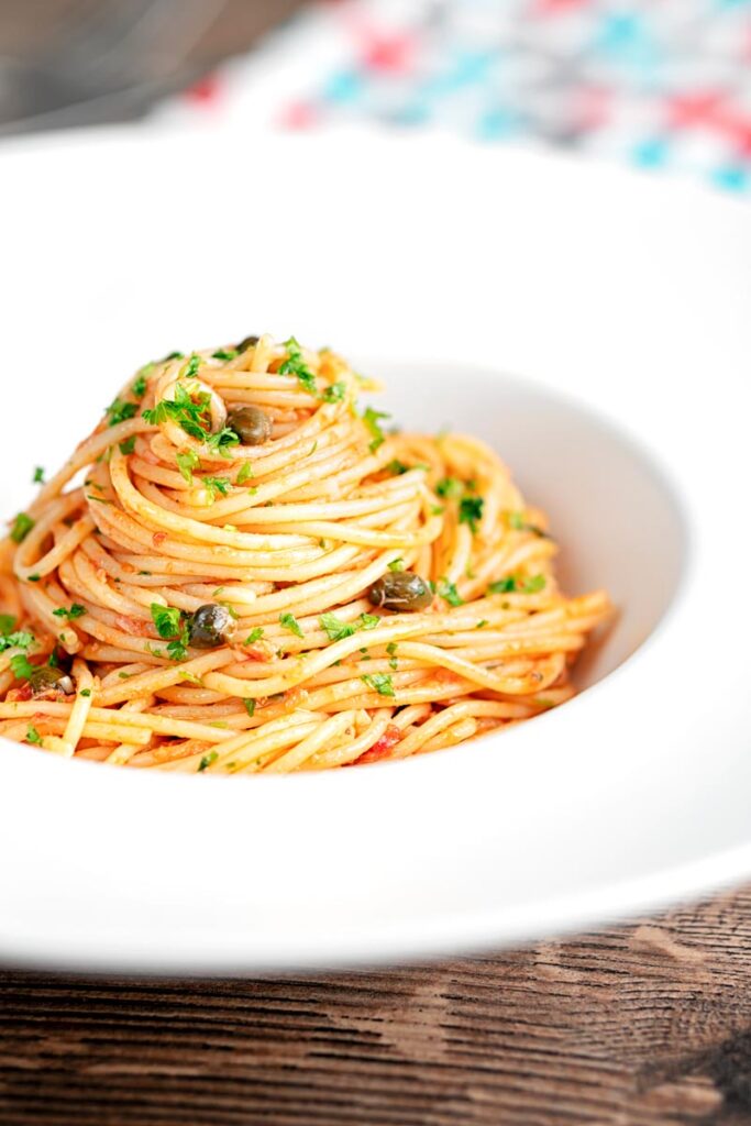 Portrait image of a pile caper, tomato and tuna spaghetti served in a white pasta bowl