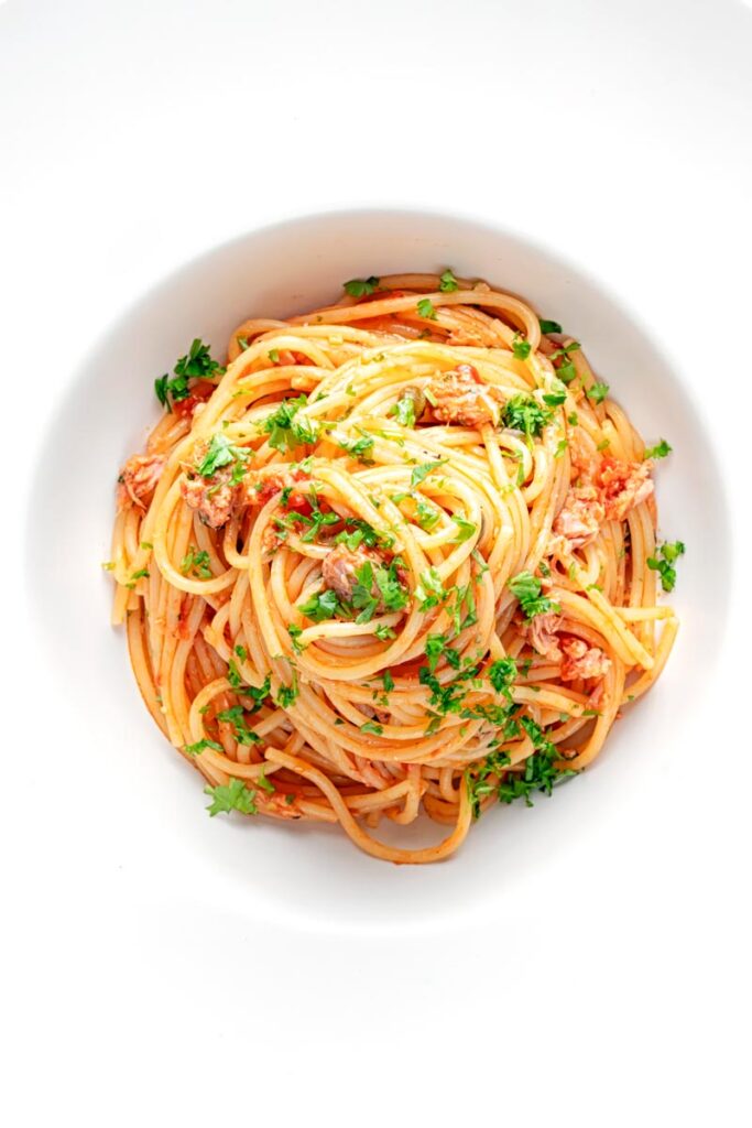 Portrait overhead image of a pile caper, tomato and tuna spaghetti served in a white pasta bowl