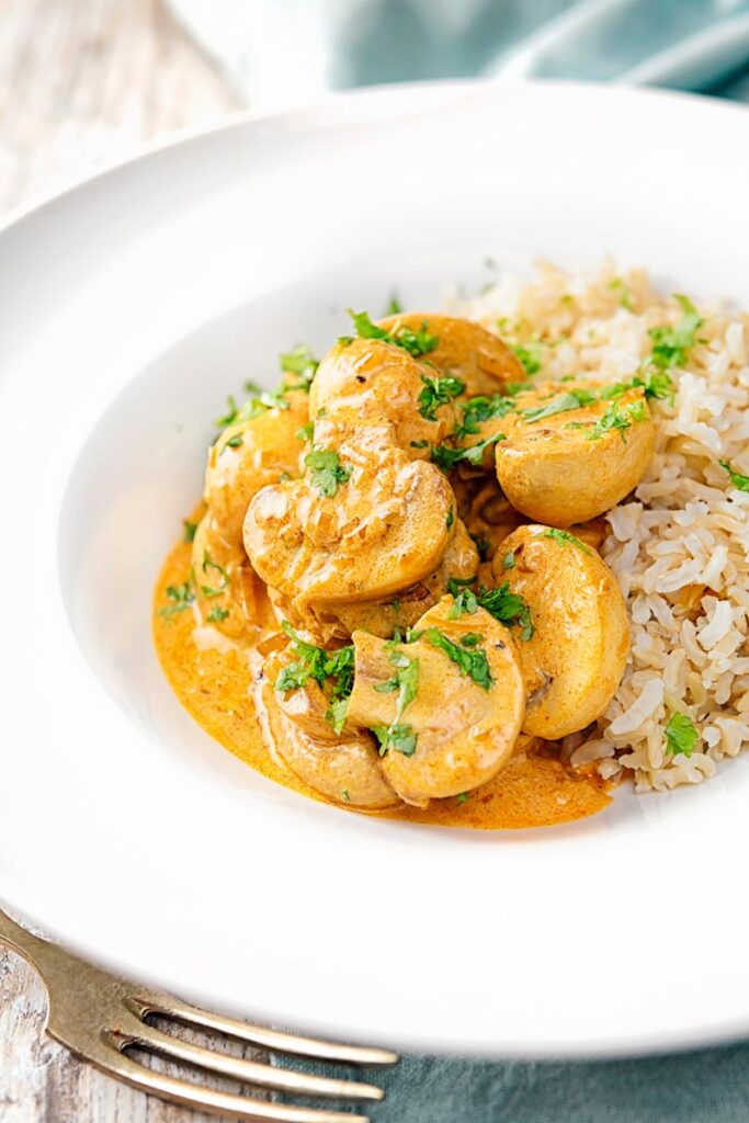 Portrait image of a vegetarian mushroom stroganoff served with wholegrain rice in a white bowl