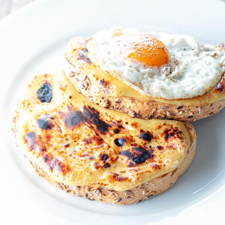 Square image of welsh rarebit with a fried egg, AKA buck rarebit served on a white plate