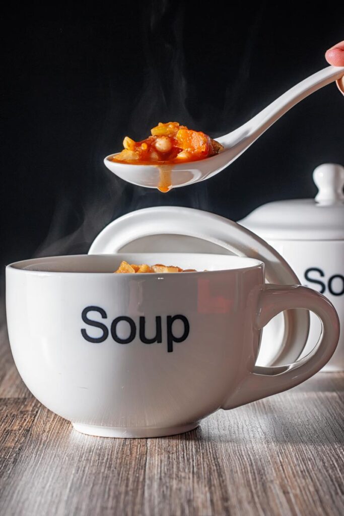 Portrait image of a spoonful of winter vegetable soup being taken a steaming soup cup