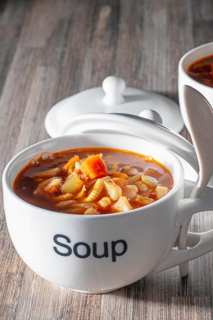Portrait image of a winter vegetable soup served in a large cup with soup printed on the front