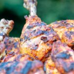 Portrait close up image of a BBQ tandoori chicken drumstick with surrounded by out of focus chicken