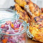 Portrait image of kachumber salad in a jar with out of focus tandoori chicken behind it