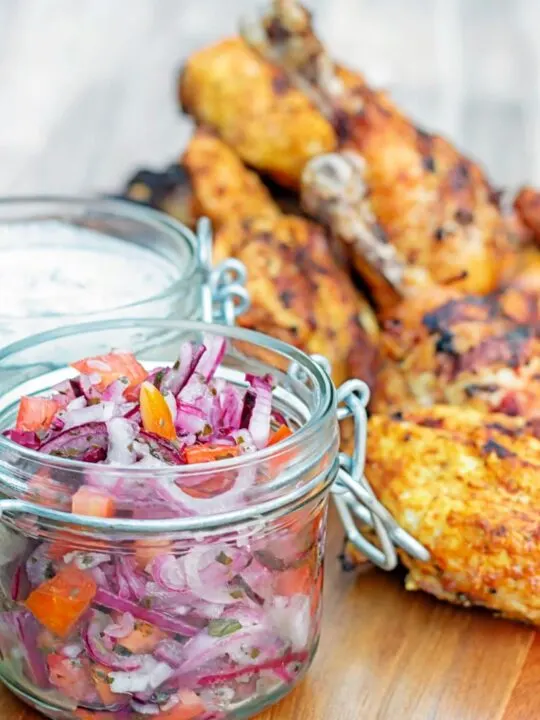 Portrait image of kachumber salad in a jar with out of focus tandoori chicken behind it