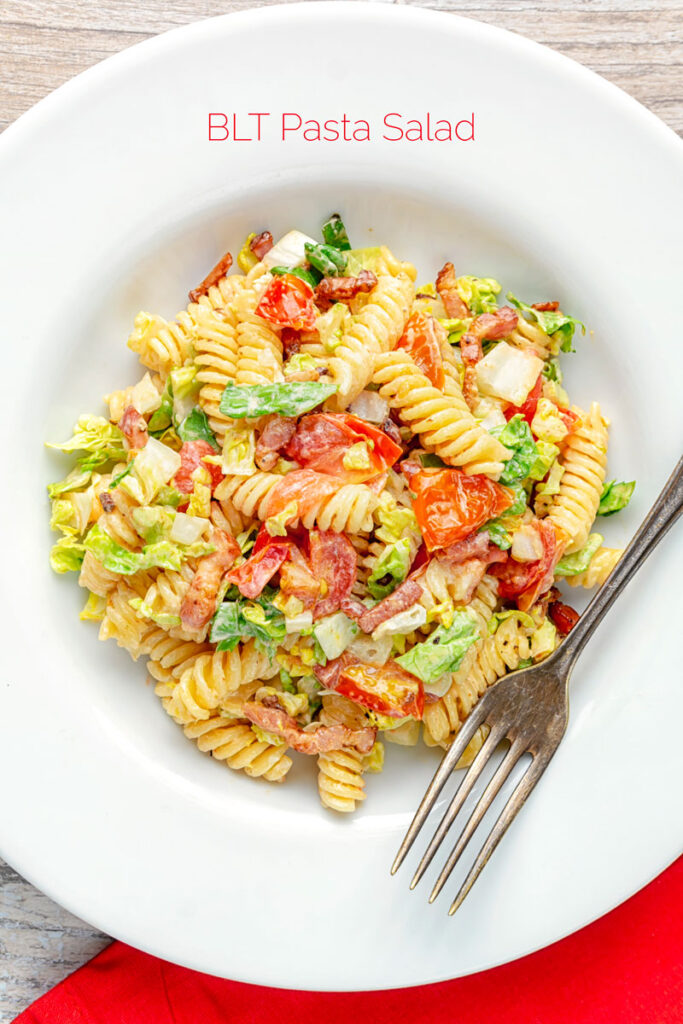 Portrait overhead image of a BLT pasta salad using fusilli pasta served in a shallow white bowl with text overlay