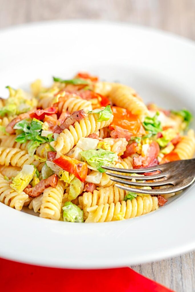 Portrait image of a BLT pasta salad using fusilli pasta served in a shallow white bowl