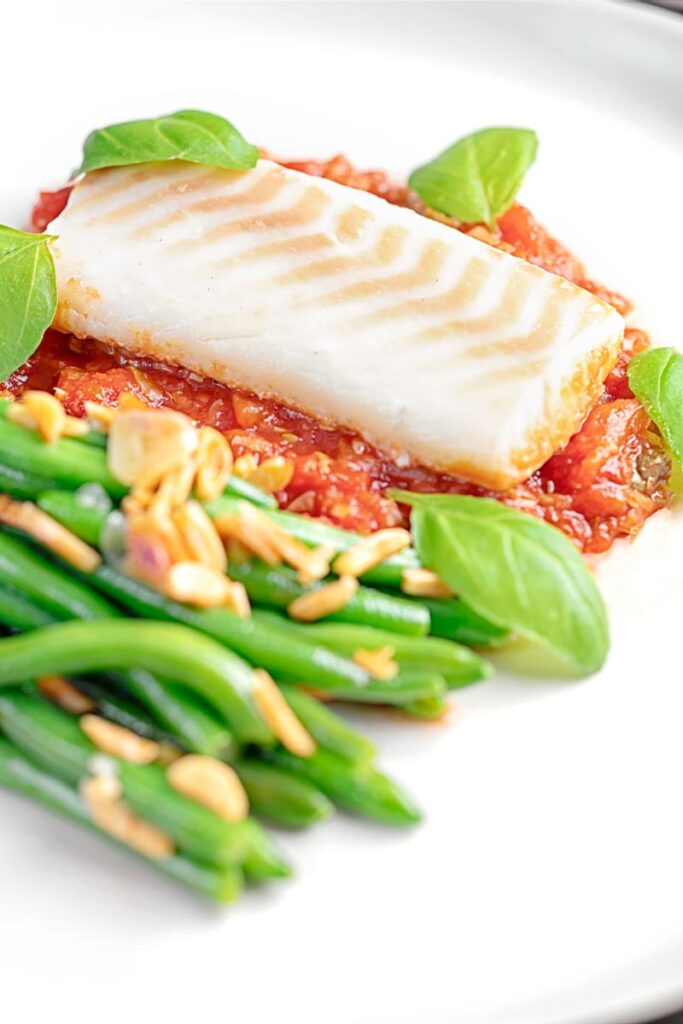 Portrait image of baked cod fillet on tomato sauce with green beans and fresh basil