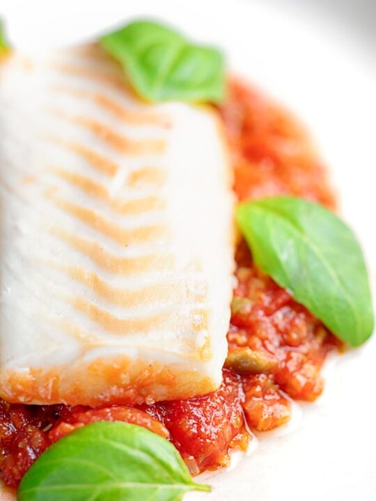 Portrait close up image of baked cod fillet on tomato sauce with green beans and fresh basil