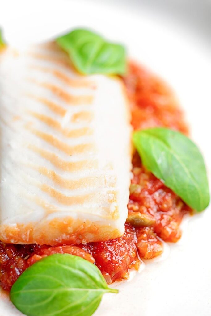 Portrait close up image of baked cod fillet on tomato sauce with green beans and fresh basil