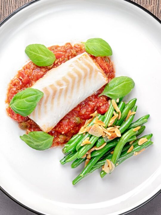 Portrait overhead image of baked cod fillet on tomato sauce with green beans and fresh basil