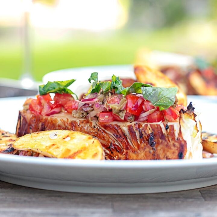 Square image of a balsamic cabbage heart steak served with tomato salad and potato wedges.