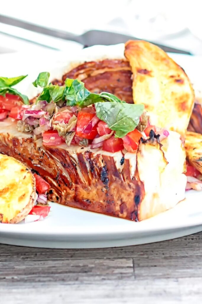 Portrait close image of a balsamic cabbage heart steak served with tomato salad and potato wedges.