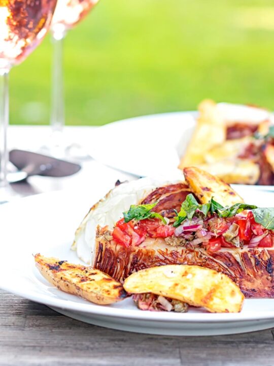 Portrait image of a balsamic cabbage heart steak served with tomato salad and potato wedges.