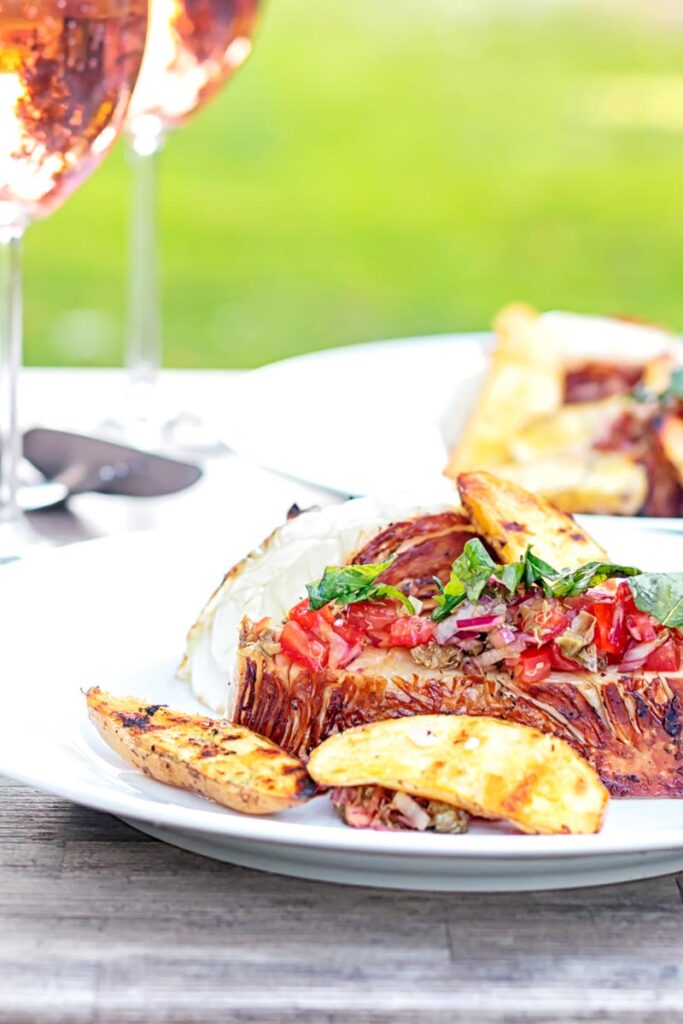 Portrait image of a balsamic cabbage heart steak served with tomato salad and potato wedges.