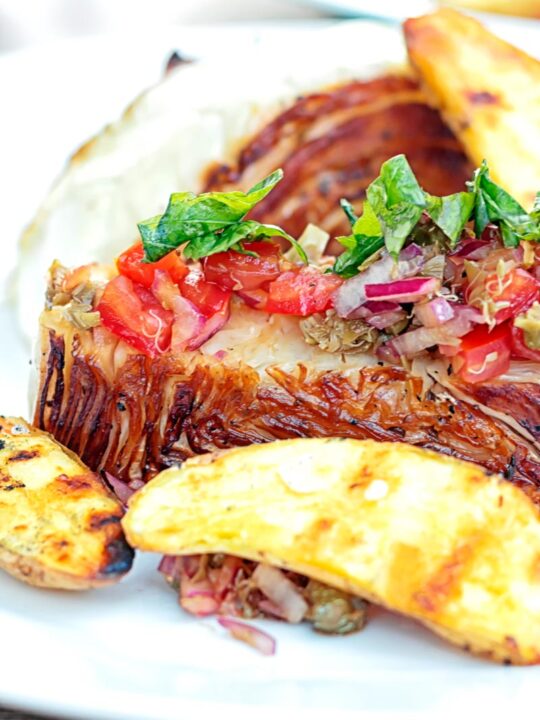 Portrait close in image of a balsamic cabbage heart steak served with tomato salad and potato wedges.