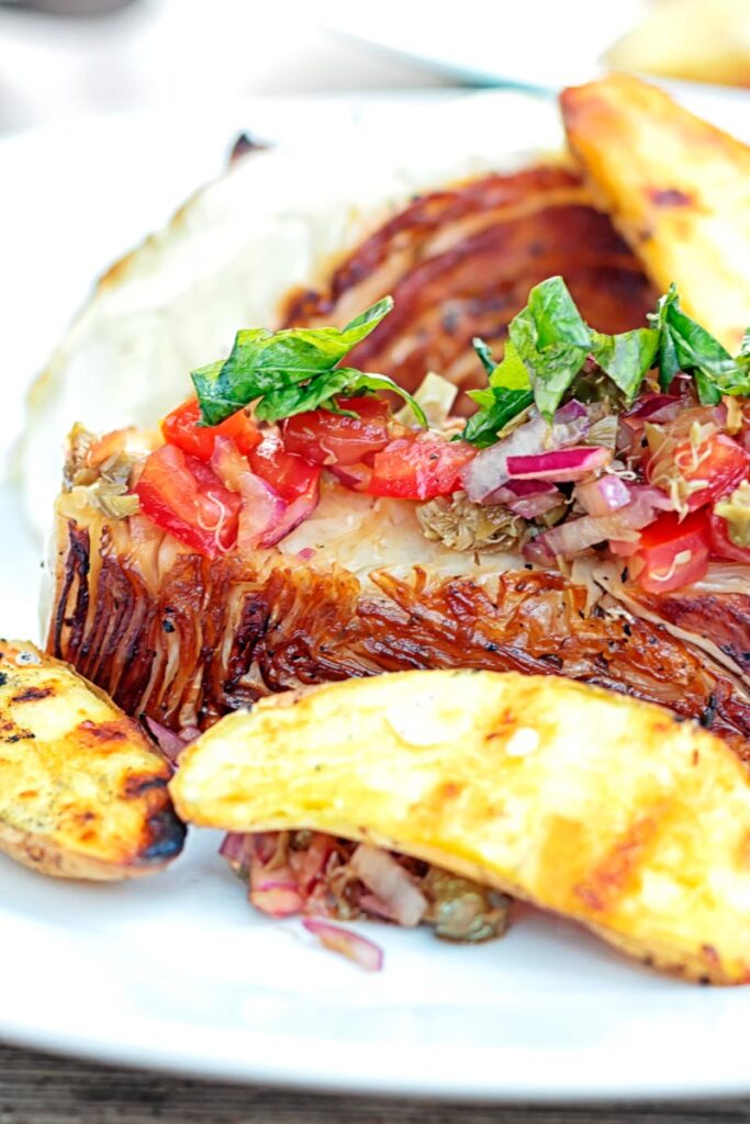 Portrait close in image of a balsamic cabbage heart steak served with tomato salad and potato wedges.