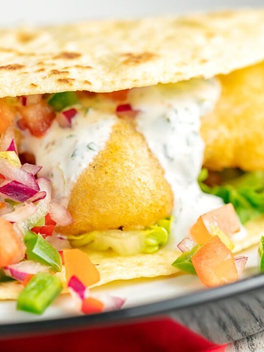 Portrait close up image of beer battered cod fish fish tacos served in a corn tortilla with a coriander crema