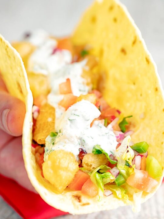 Portrait image of beer battered cod fish tacos served in a corn tortilla with a coriander crema