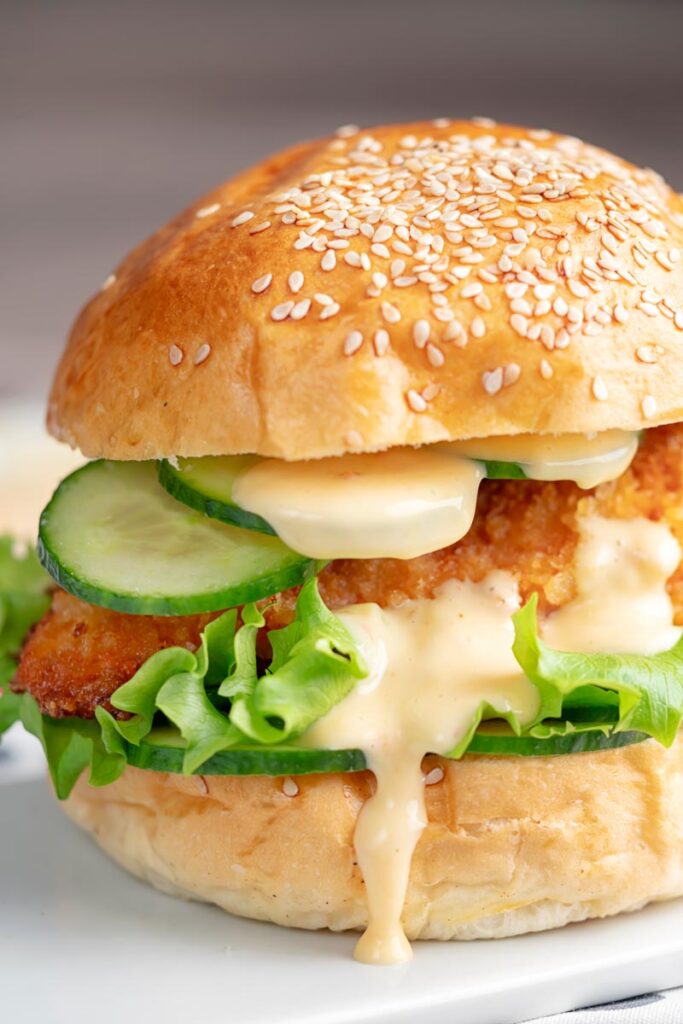 Portrait image of a chicken breast burger with lettuce and cucumber and a dollop of chilli and lime mayo