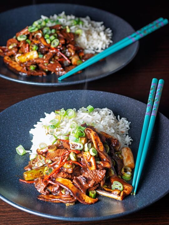 Portrait image of a streaming hot Chinese beef and shiitake mushroom stir fry served on two black plates
