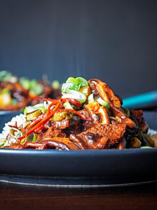 Portrait image of a streaming hot Chinese beef and shiitake mushroom stir fry served on a dark plate