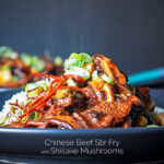 Portrait image of a streaming hot Chinese beef and shiitake mushroom stir fry served on a dark plate with text overlay
