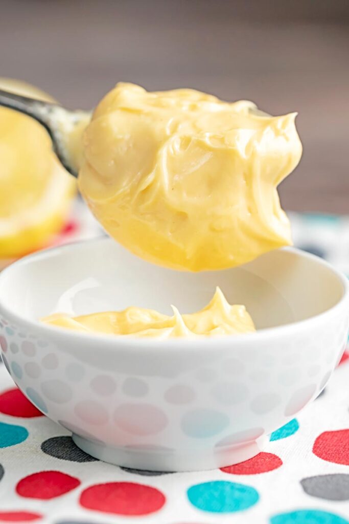 Portrait image of thick classic homemade mayonnaise being served into a white bowl from a spoon