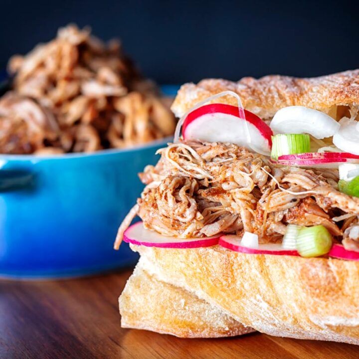 Square close up image of an easy slow cooker pulled pork sandwich on a ciabatta style loaf with pickles