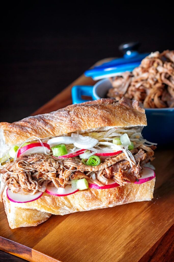 Portrait up image of a slow cooker pulled pork sandwich on a ciabatta style loaf with pickles
