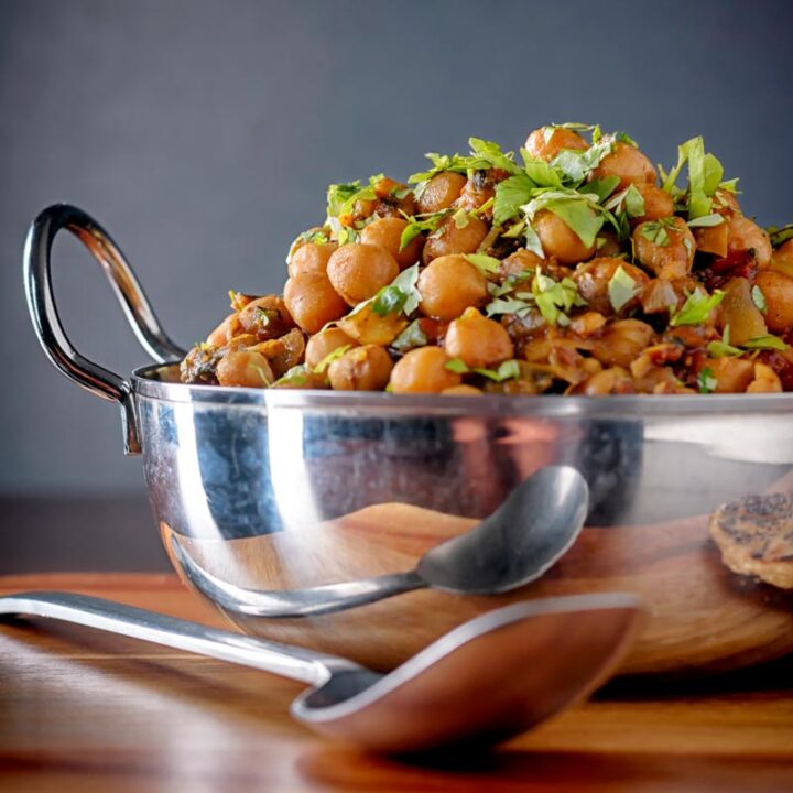 Square image of a chole or Indian chickpea curry garnished with chopped coriander served in a karahi