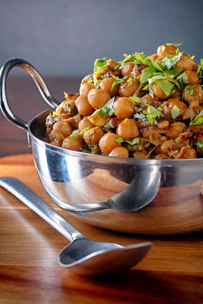 Portrait image of a chole or Indian chickpea curry garnished with chopped coriander served in a karahi