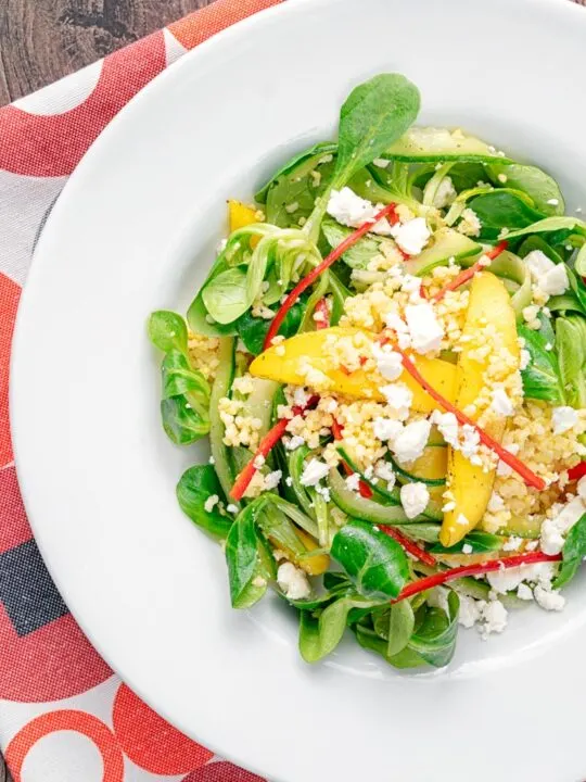 Portrait overhead image of a main course mango salad featuring lambs lettuce with feta cheese, millet and chilli shreds