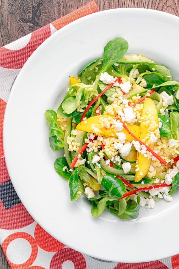 Portrait overhead image of a main course mango salad featuring lambs lettuce with feta cheese, millet and chilli shreds