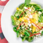 Portrait overhead image of a main course mango salad featuring lambs lettuce with feta cheese, millet and chilli shreds with text overlay