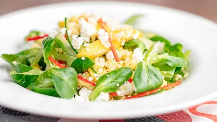 Landscape image of a main course mango salad featuring lambs lettuce with feta cheese, millet and chilli shreds