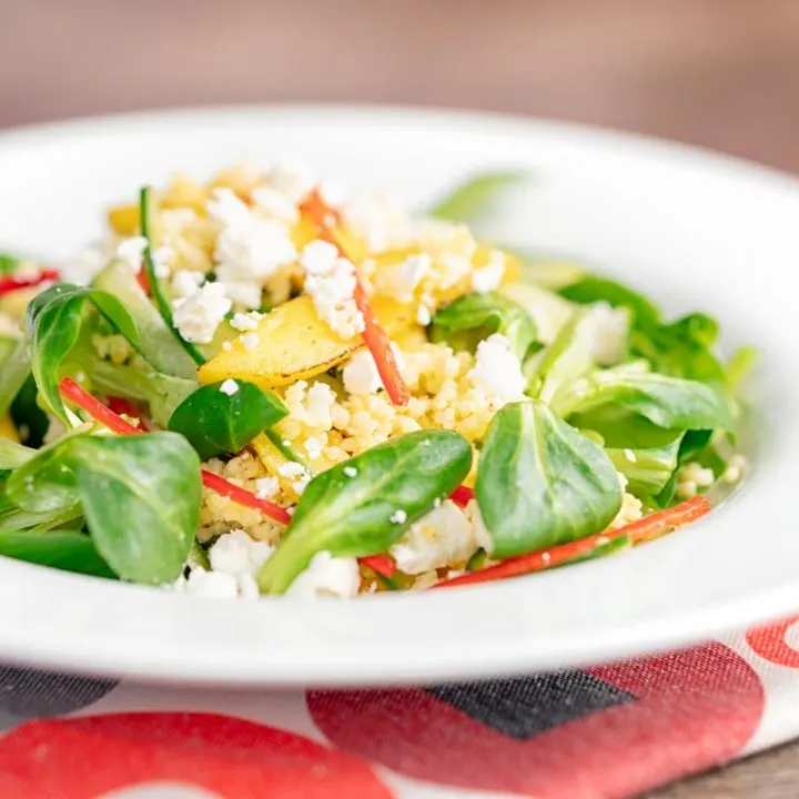 Square image of a main course mango salad featuring lambs lettuce with feta cheese, millet and chilli shreds