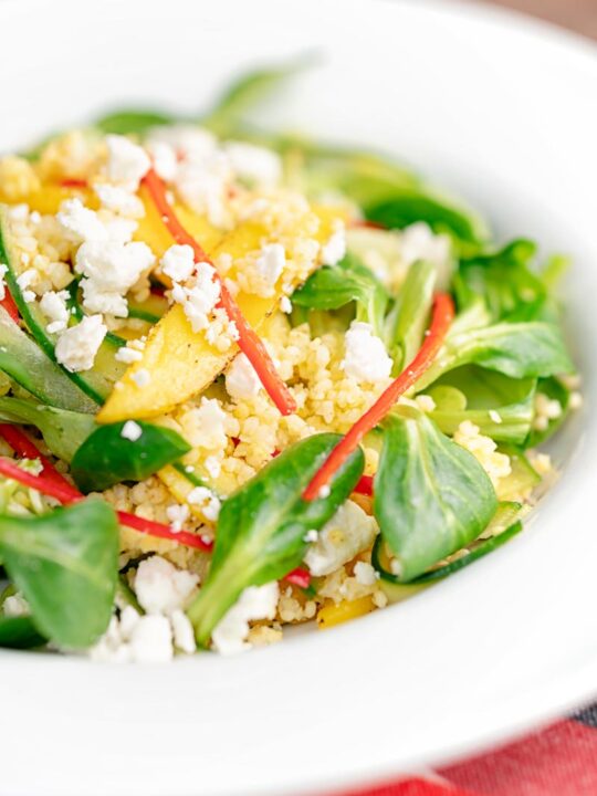 Portrait image of a main course mango salad featuring lambs lettuce with feta cheese, millet and chilli shreds