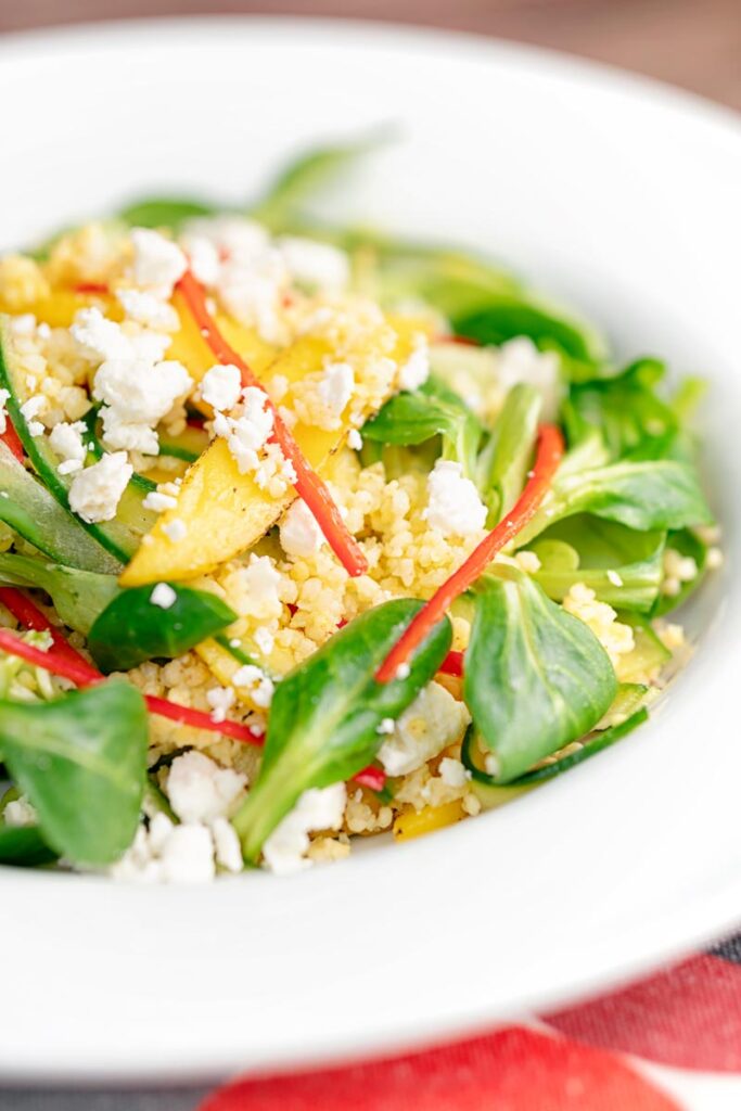 Portrait image of a main course mango salad featuring lambs lettuce with feta cheese, millet and chilli shreds