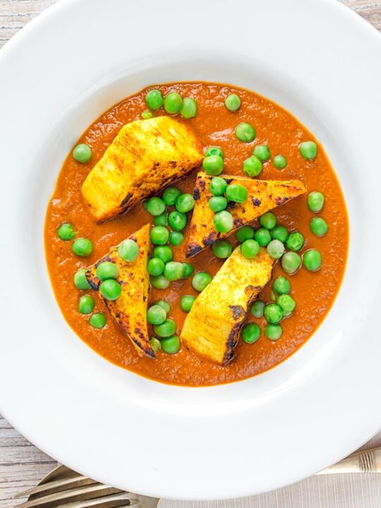 Portrait overhead image of a matar paneer curry in a masala sauce served in a white bowl